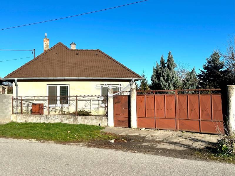 A family house in Horné Saliby with a gabled roof and a large metal gate.