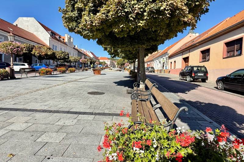 City park in the historic center of Svätý Jur on Prostredná Street with benches and trees.