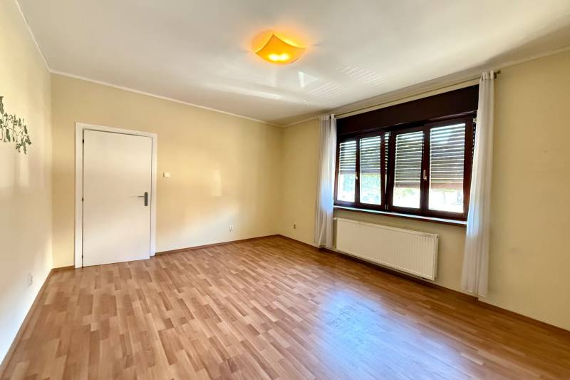 A spacious room in a family house with a wood-decor floor and a large window.