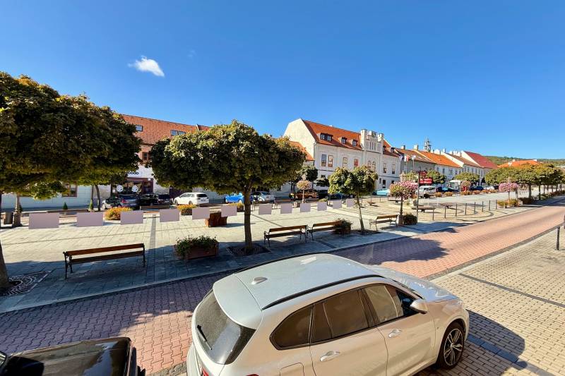 The center of Svätý Jur on Prostredná Street with cars and trees, historic houses in the background.