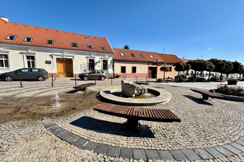 The fountain with benches on Prostredná Street in Svätý Jur, lined with historic buildings.