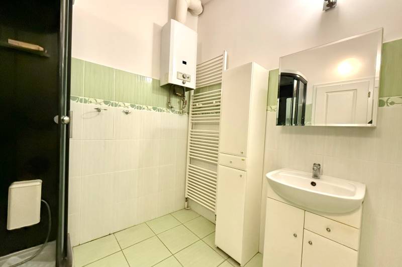 Bathroom in a family house with tiles, a sink, a mirror, and a water heater.