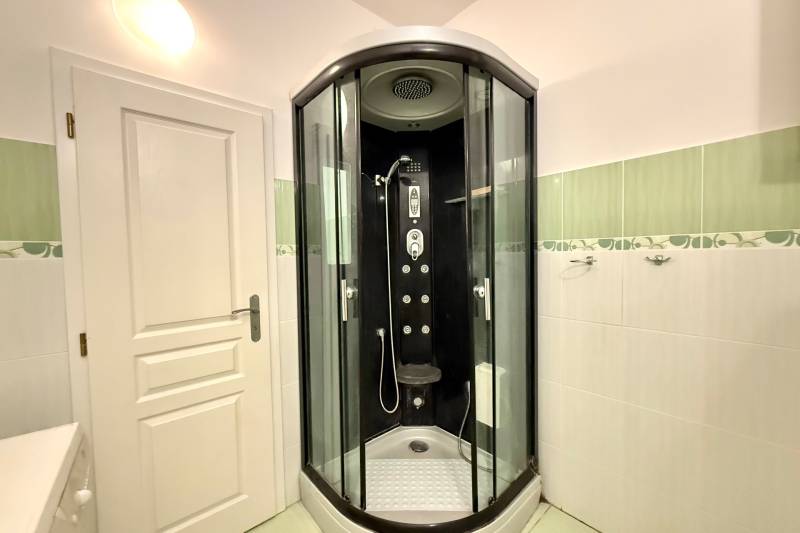 A shower enclosure in the bathroom of a family house with white and green tiles.