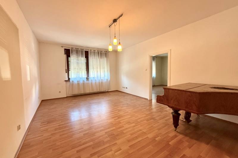 A room in a family house with a wooden decor floor, curtains, and a piano.
