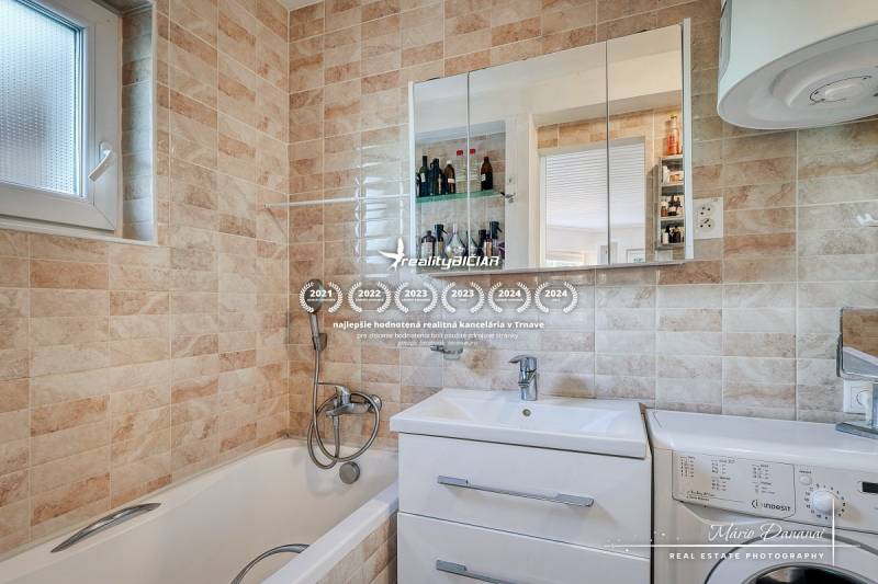 Bathroom with a bathtub, sink, and mirror in a family house, tiled with beige tiles.