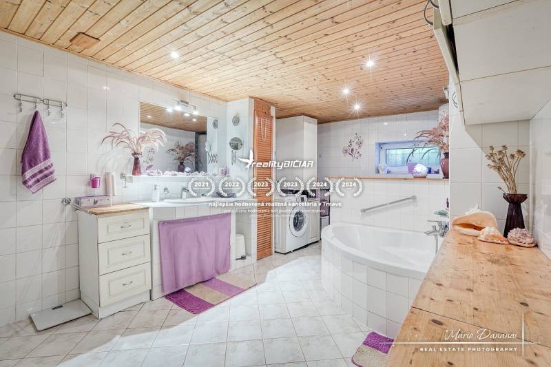 A bathroom in a cottage with white tiles, a bathtub, and accessories in lilac shade.