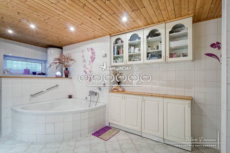 A bathroom in a family house with a corner bathtub and a wooden ceiling, decorated tiles.