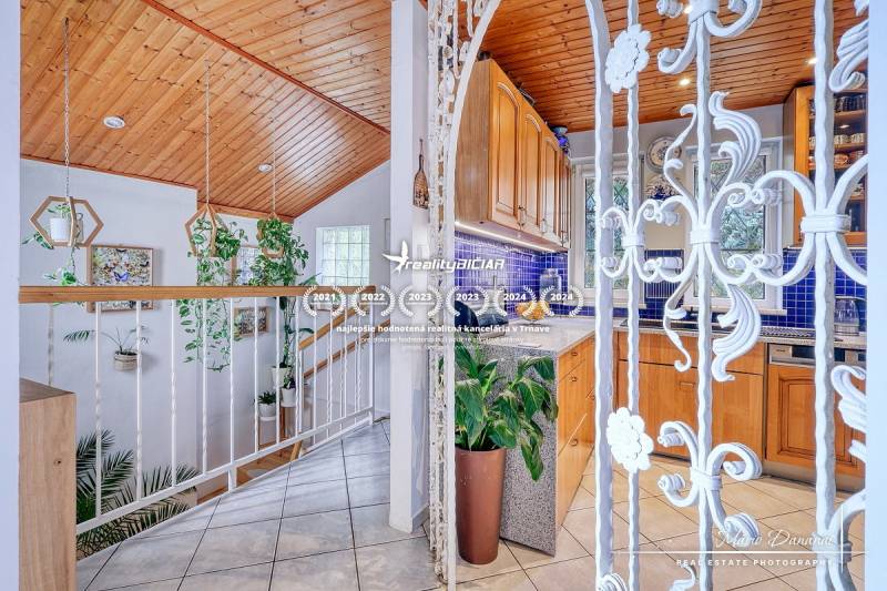 The interior of a family house with a wooden ceiling decor, white railing, and green plants.