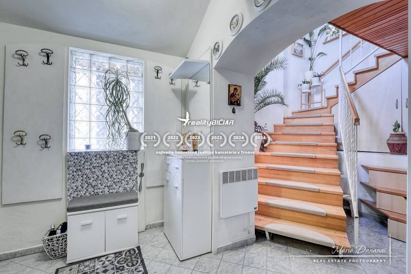 A cottage with a wooden staircase, white furniture, and a plant; interior with a wood-decor floor.
