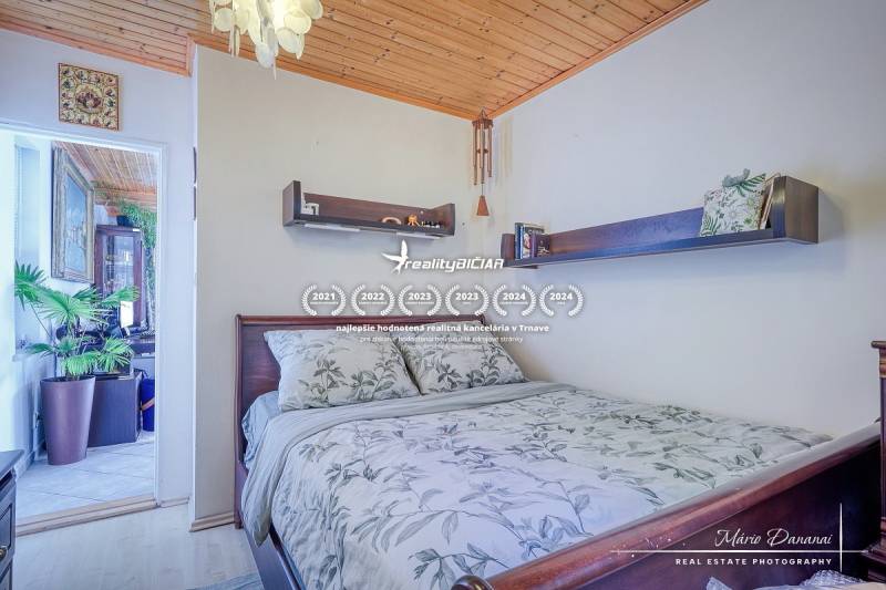 Bedroom in a cabin with a wooden ceiling, flowers, and shelves above the bed.