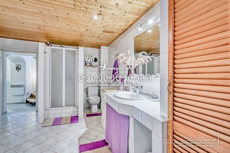 Bathroom in a family house with tiles, a shower corner, a toilet, and a wooden ceiling.