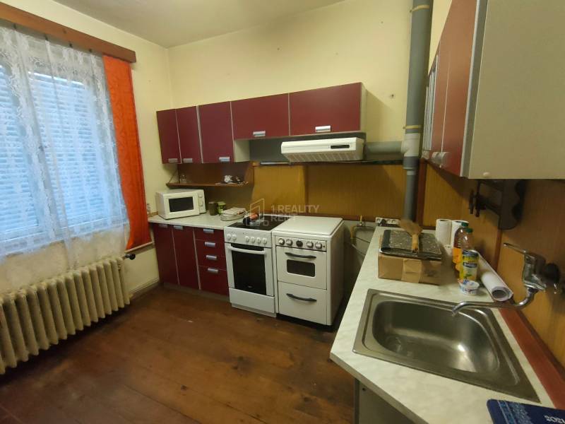 A kitchen in a family house with a wood-patterned floor, red cabinets, and white appliances.