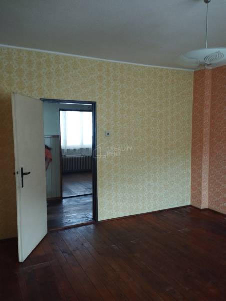 A family house with a wooden decor floor and wallpapered walls, doors leading to another room.