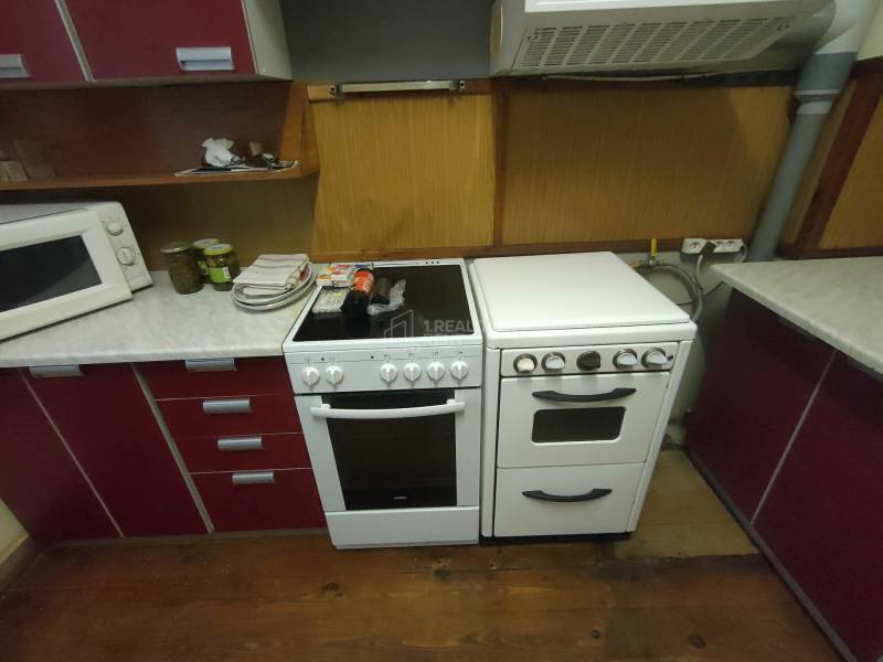 A kitchen in a family house with an oven, a cooktop, a microwave, and a floor with a wooden decor.