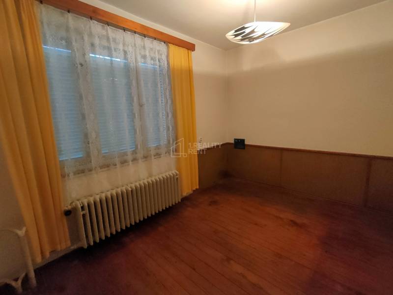 A room in a family house with a wooden decor floor, curtains, and a radiator.