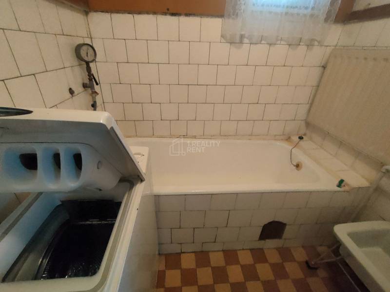 A bathroom in a family house with a bathtub and a washing machine, tiled with white tiles.