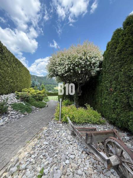 The exterior of the villa in Súľov-Hradná with a pathway, greenery, and a wooden cart.