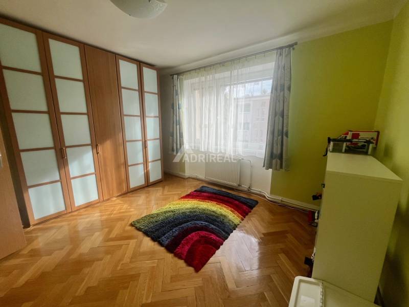 A room in a 3-room apartment with a wooden decor floor and a colorful carpet.