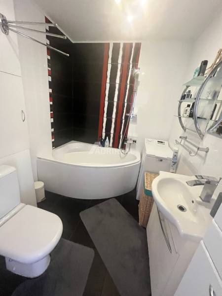 A bathroom in a 3-room apartment with a bathtub, black tiles, and a washing machine.