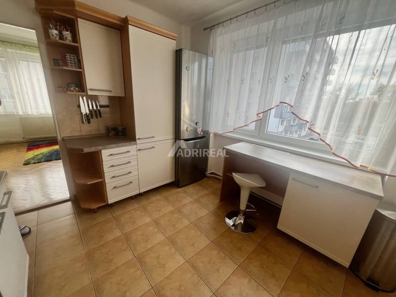 A kitchen in a 3-room apartment with tiles, white furniture, and a large window.