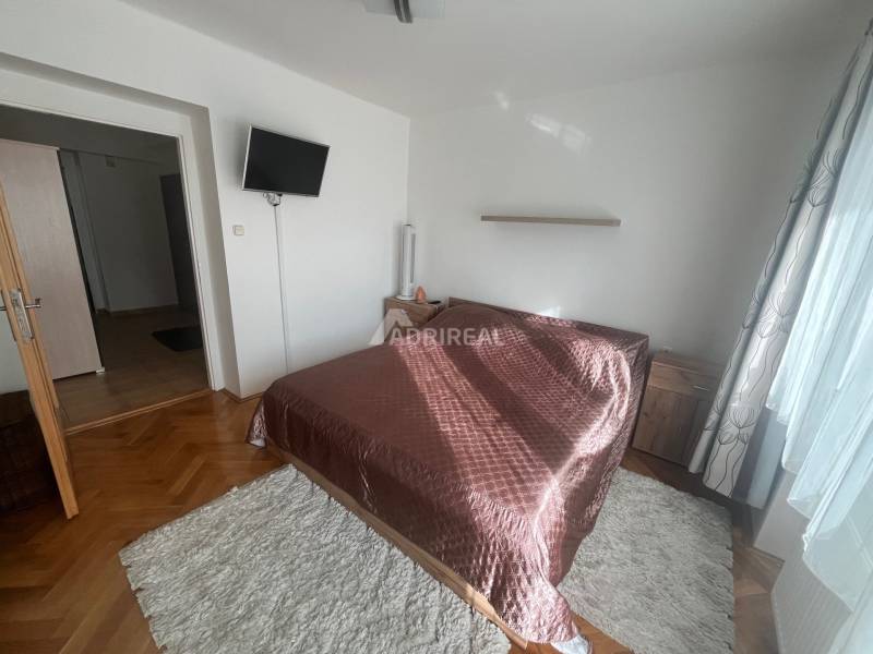A bedroom in a three-room apartment with a wooden decor floor, a bed, and a television.