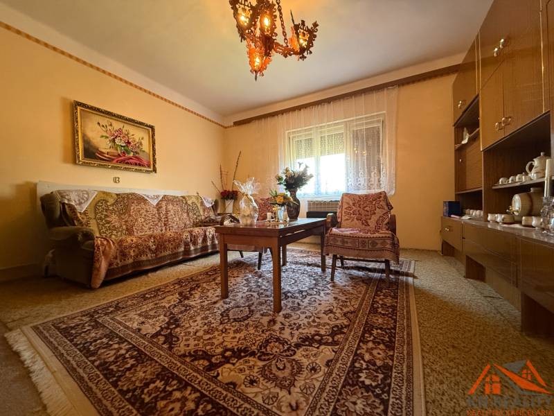 Living room in a family house with a carpet, sofa, chair, and chandelier.
