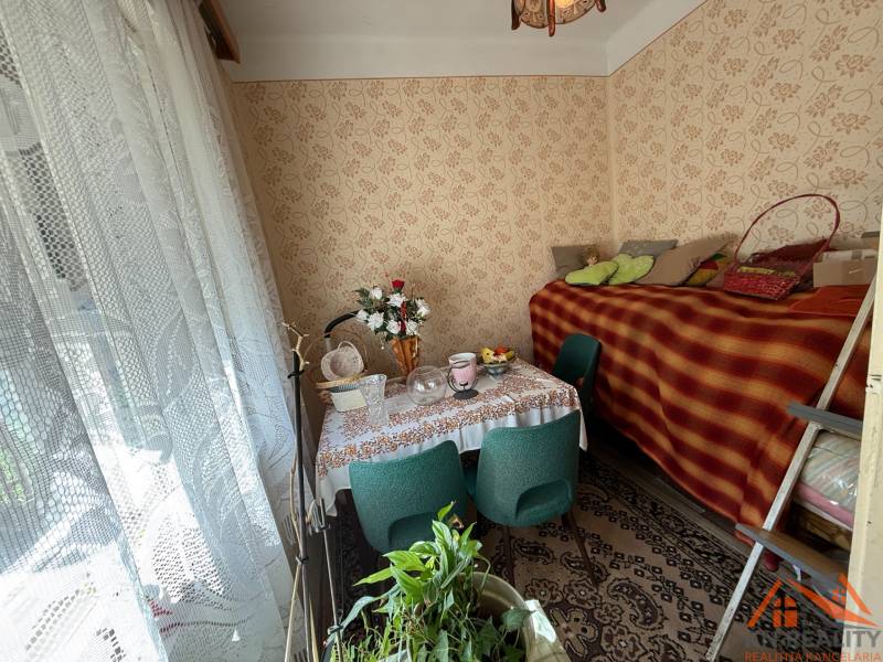 Interior of a family house with flowers, a table, and a bed with a carpet.