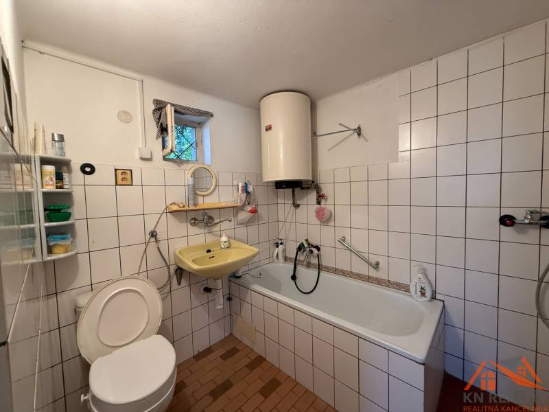 A bathroom in a family house with a bathtub, a yellow sink, tiles, and a boiler on the wall.