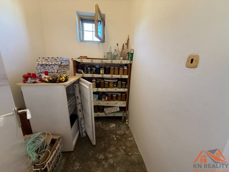 A pantry in a family house with a freezer, a shelf for preserves, and a small window.