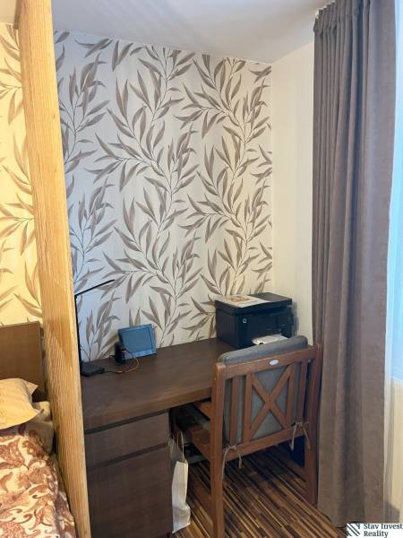 A workspace in a 2-room apartment with leaf-patterned wallpaper and dark furniture.