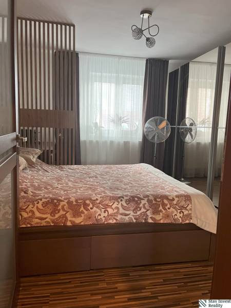 Bedroom in a two-room apartment with a double bed, lamp, and windows with heavy curtains.