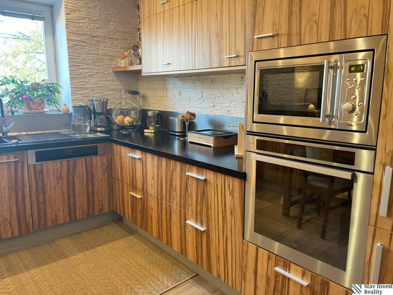 A kitchen with wooden cabinets, a built-in oven, and a window in a 2-room apartment.