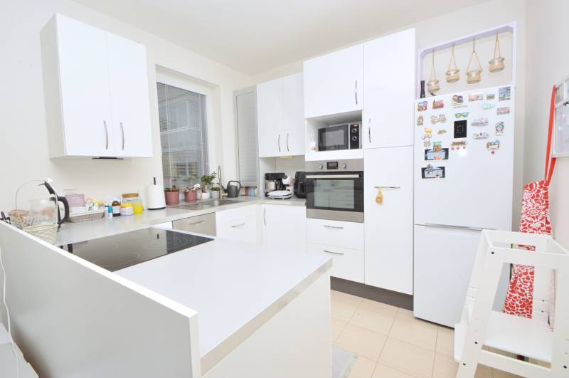 A bright kitchen in a three-room apartment, with white cabinets and appliances.