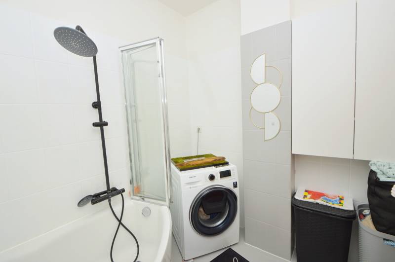 A bathroom in a 3-room apartment with a bathtub, washing machine, and a modern shower enclosure.