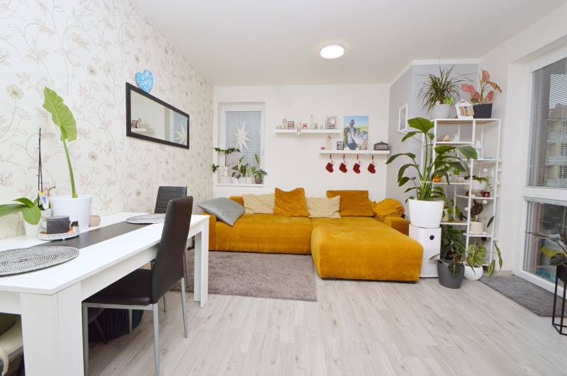 Living room with a mustard couch, white table, and wood-patterned floor, 3-room apartment.