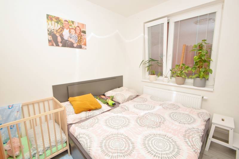 A bedroom in a three-room apartment with a bed, a baby crib, and plants on the windowsill.