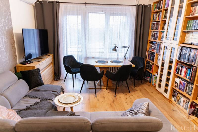 Living room with a sofa, dining table, television, and bookshelf. Floor with wood decor.