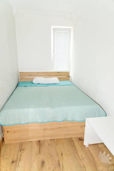A bed with a blue blanket on a wooden floor, 3-room apartment.