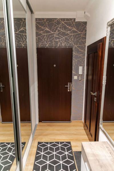 Entrance hallway in a 3-room apartment with a wooden decor floor and a mirrored wardrobe.