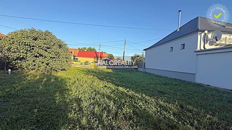 Plots - housing in Kameničná with greenery and a neighboring house under the blue sky.