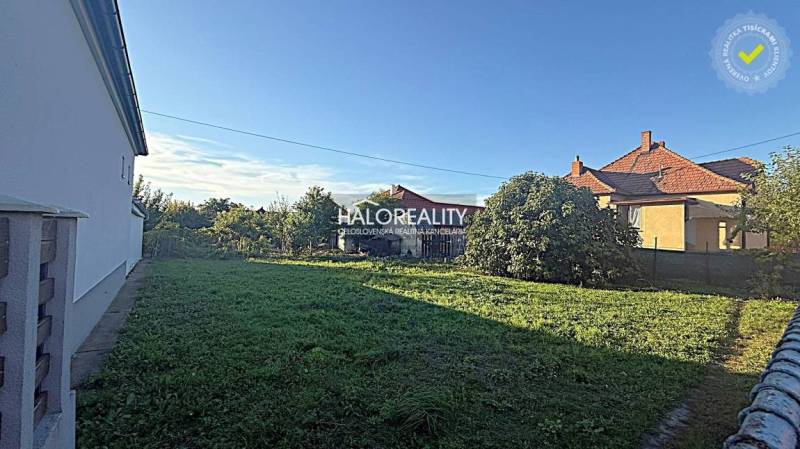 Plots for residential use in Kameničná with grassy vegetation, houses, and a blue sky.