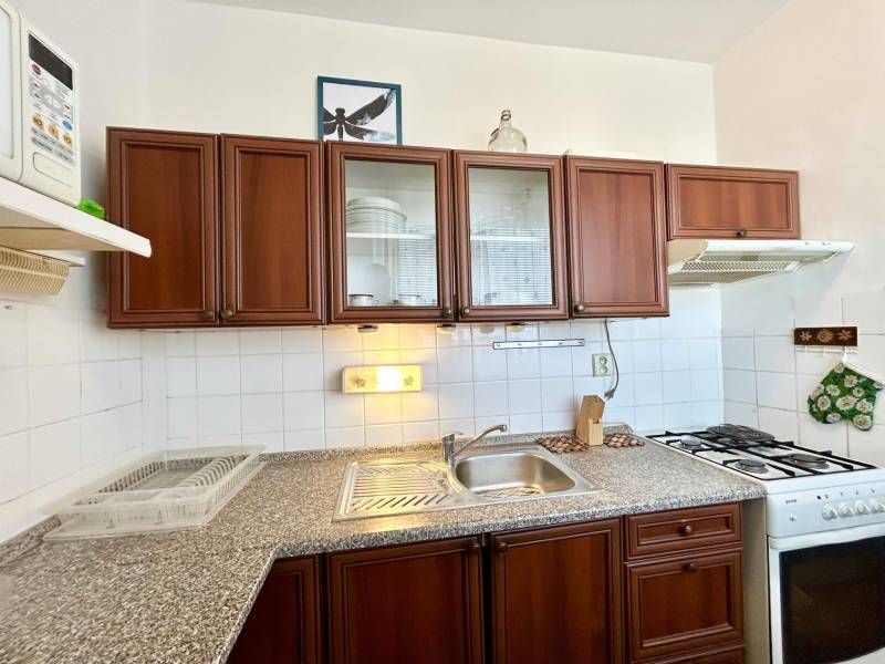 A kitchen unit in a 2-room apartment with dark wooden cabinets and white tiles.