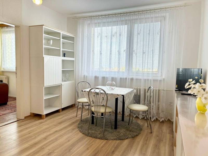 Dining room in a 2-room apartment with wood-patterned flooring and white furniture.