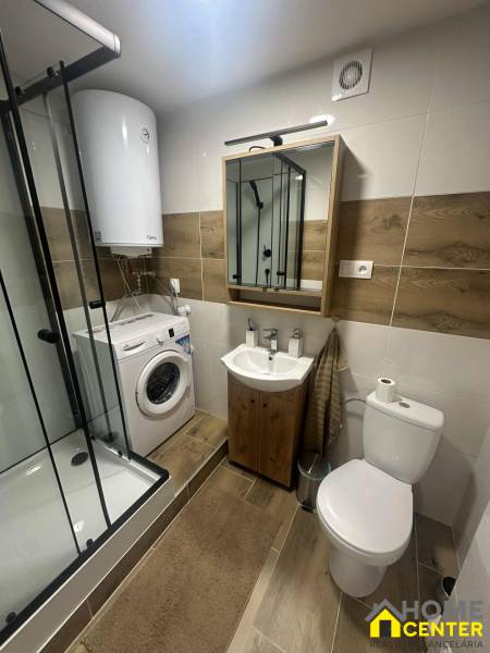 Bathroom in a studio apartment with a washing machine, shower cabin, and floor with wood decor.