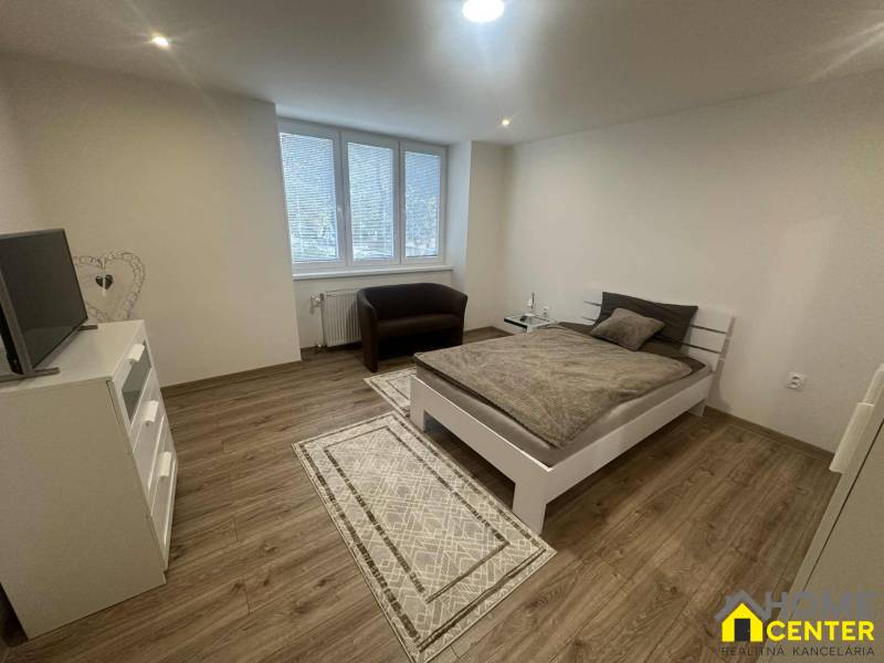 A bright room with a bed, chair, television, and wood-decor flooring in a studio apartment.