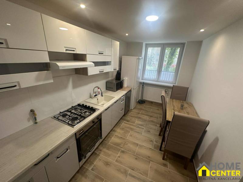 A kitchen in a studio apartment with built-in appliances and a wooden decor floor.