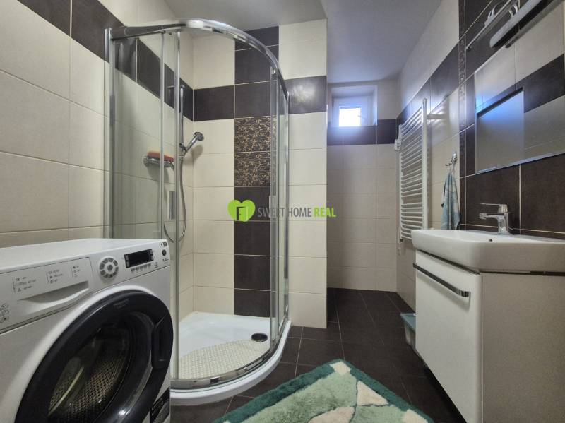 A bathroom in a family house with a washing machine, shower, and sink.