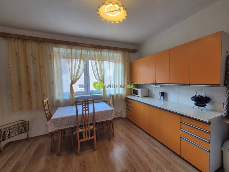 The kitchen in the family house has orange cabinets and a floor with a wood design.