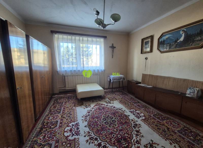 A room in a family house with carpets, wardrobes, a couch, a painting, a window with a view.