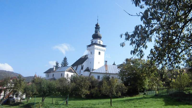 A church in Dubové surrounded by trees under a blue sky on a hillside.